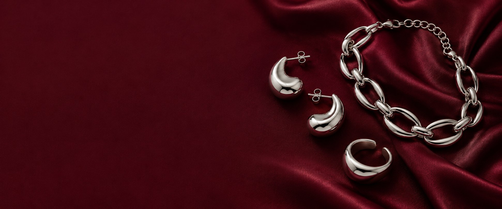 Bordo saten üzerinde gümüş renkli küpe, yüzük ve bileklik